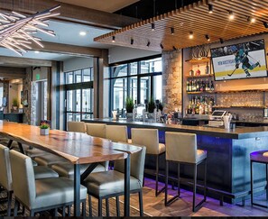 Zona de bar moderna con una mesa de madera larga, taburetes y una barra con una pantalla temática de hockey.