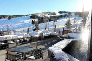 Un espace extérieur aménagé avec des tables et des chaises, offrant une vue sur une piste de ski enneigée.