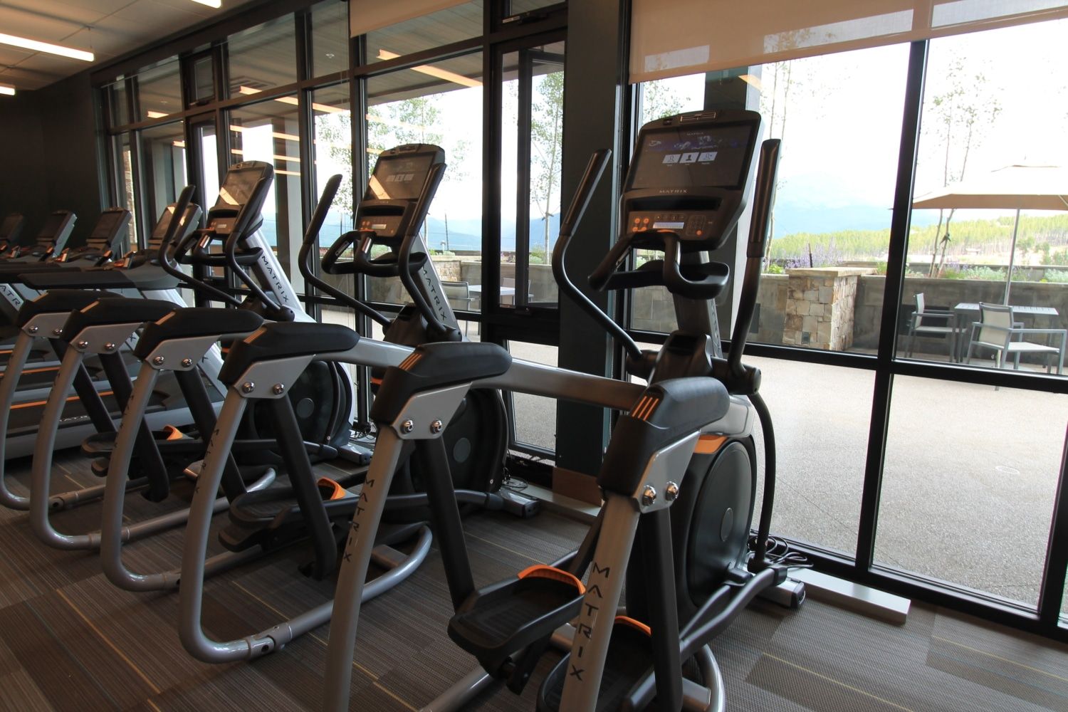 Ein Fitnessstudio mit mehreren Laufbändern, die in einer Reihe angeordnet sind, großen Fenstern und Blick ins Freie.