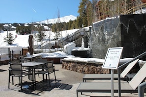 An outdoor seating area with tables and chairs, a hot tub sign, and a mountainous backdrop. - Gorgeous condo with 2 bedrooms/3 bathrooms with ski in / ski out access. (Breckenridge)