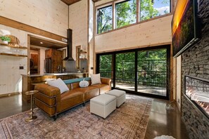A spacious living area with a leather sofa, ottomans, and a large rug. - Otter's Creek - Close to Town | Hot Tub | Fireplace | EV Charger (Blue Ridge)