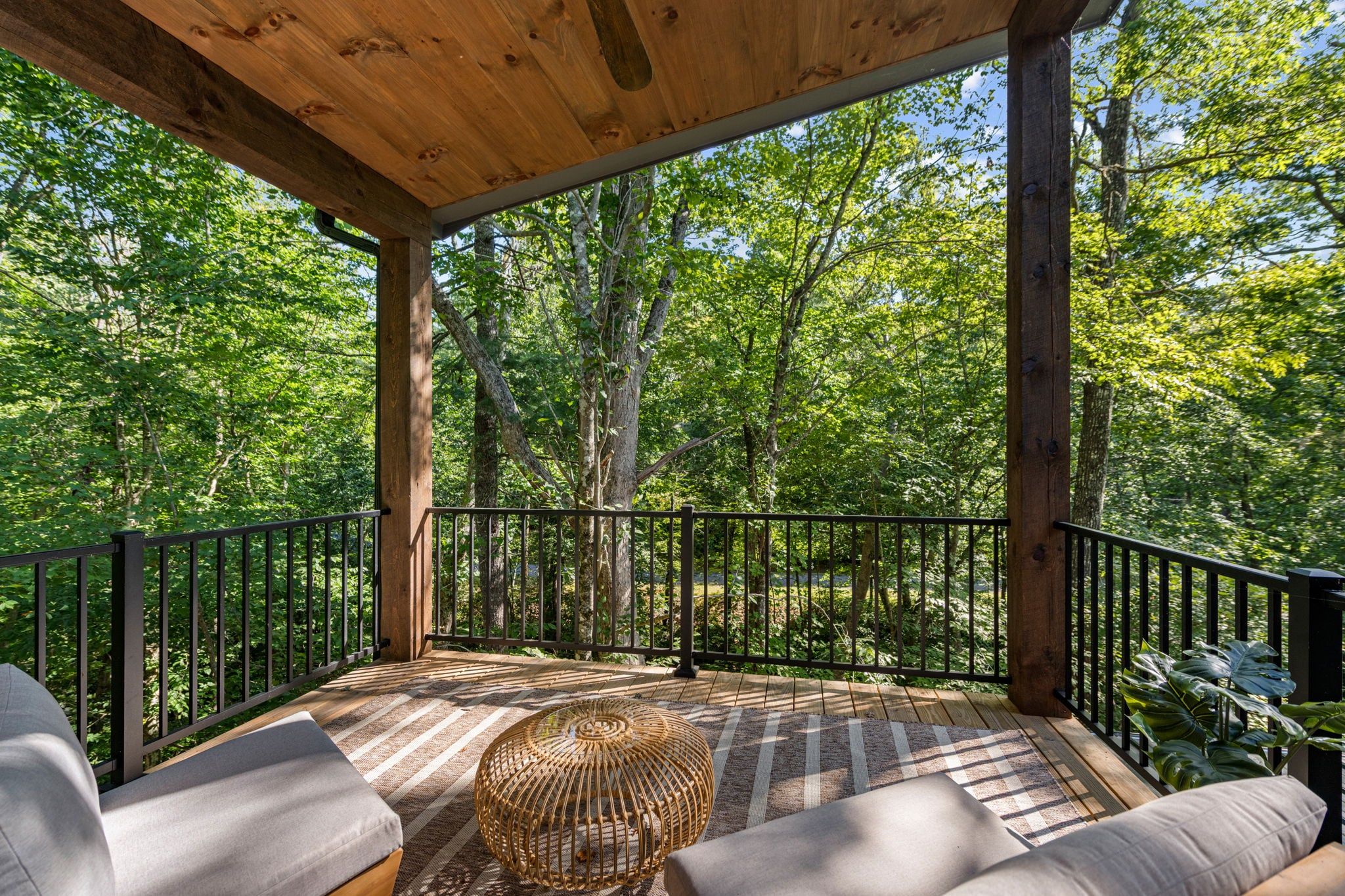 A covered outdoor deck with wooden railings, a woven basket, and cushioned seating.