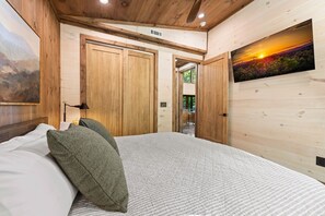 A bedroom with a bed, two doors, a painting, and a view of the outdoors. - Otter's Creek - Close to Town | Hot Tub | Fireplace | EV Charger (Blue Ridge)