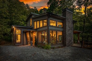 Une maison moderne à deux étages, dotée de grandes fenêtres et d’une cheminée en pierre.