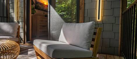 A wooden-framed sofa with grey cushions in a sunlit room with a view of greenery outside.