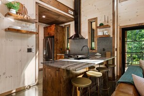 Une cuisine moderne dotée d’un îlot central, de tabourets de bar, de meubles de rangement en bois et offrant une vue sur l’extérieur.