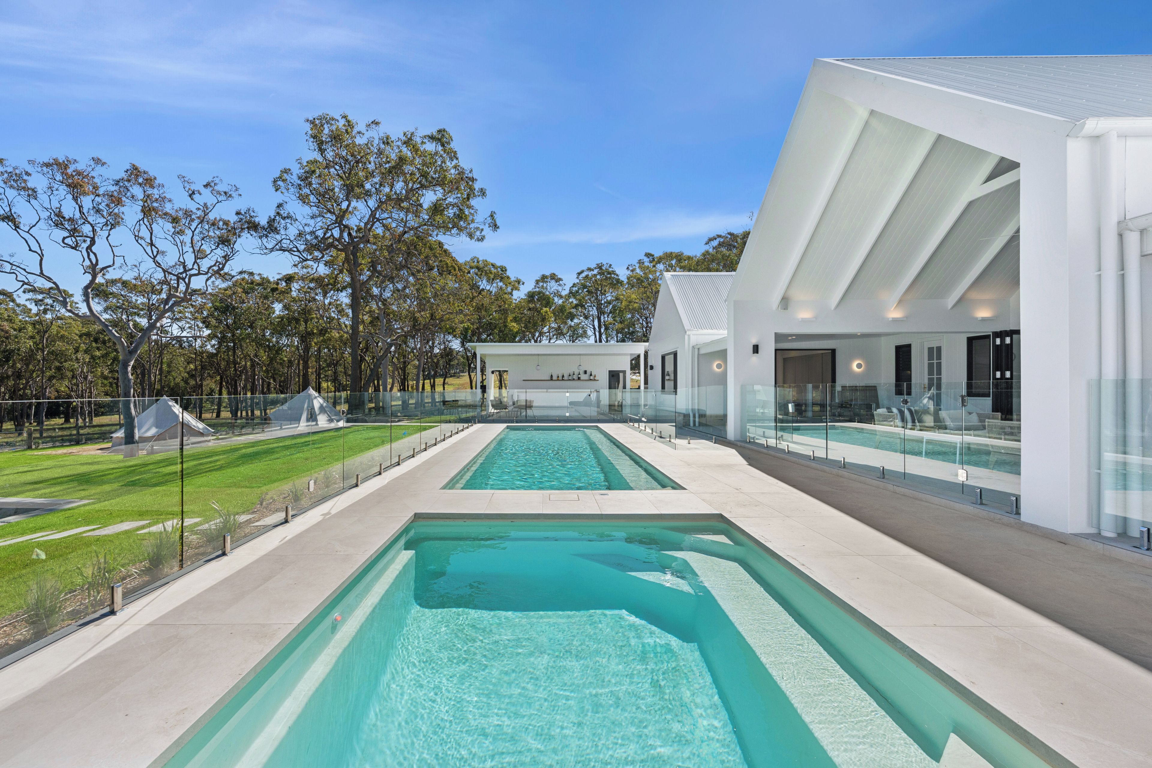 A modern pool area with clear water, surrounded by a glass fence, and adjacent to a contemporary building with large windows.