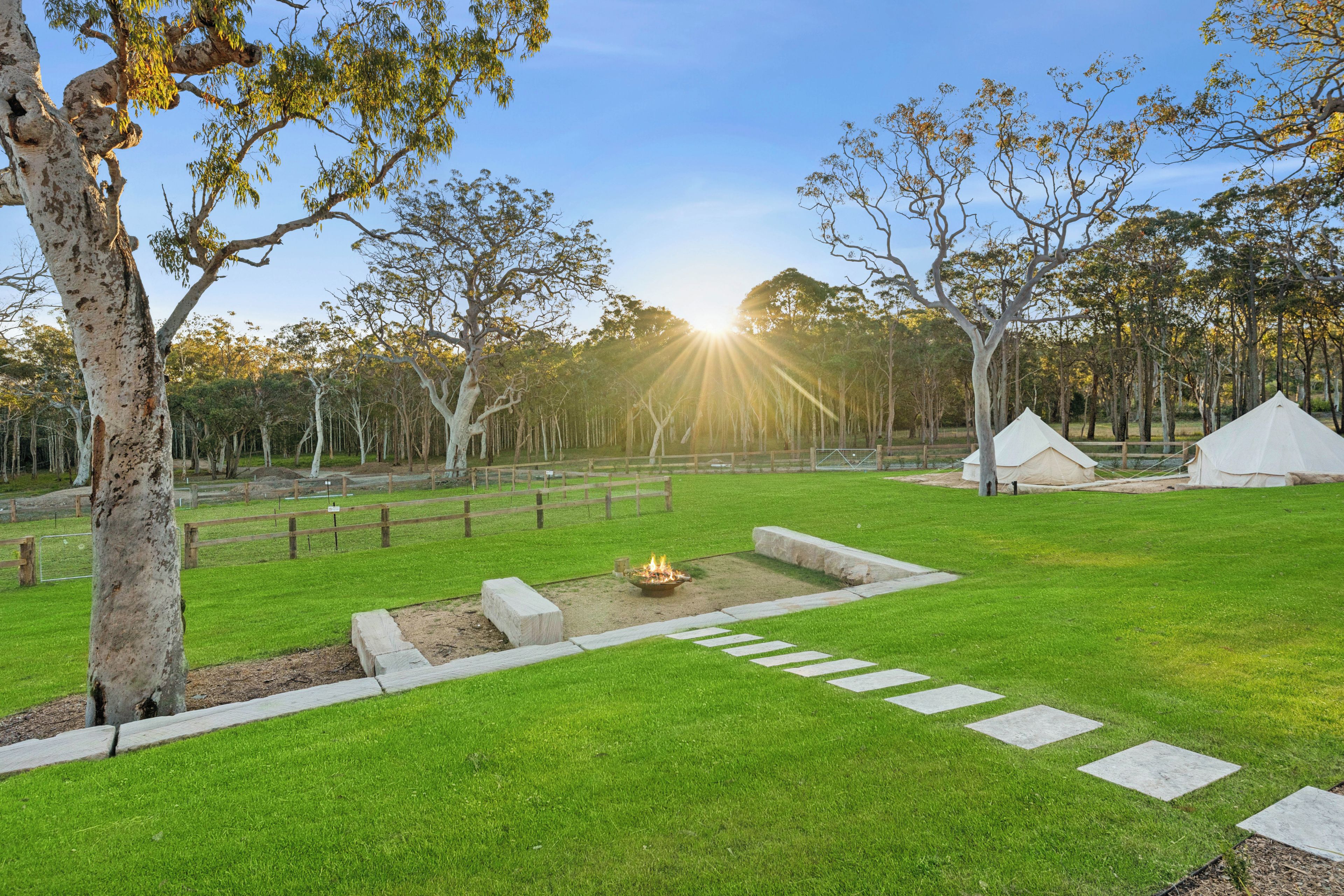 A well-maintained grassy area with a fire pit, a wooden fence, and a tent.