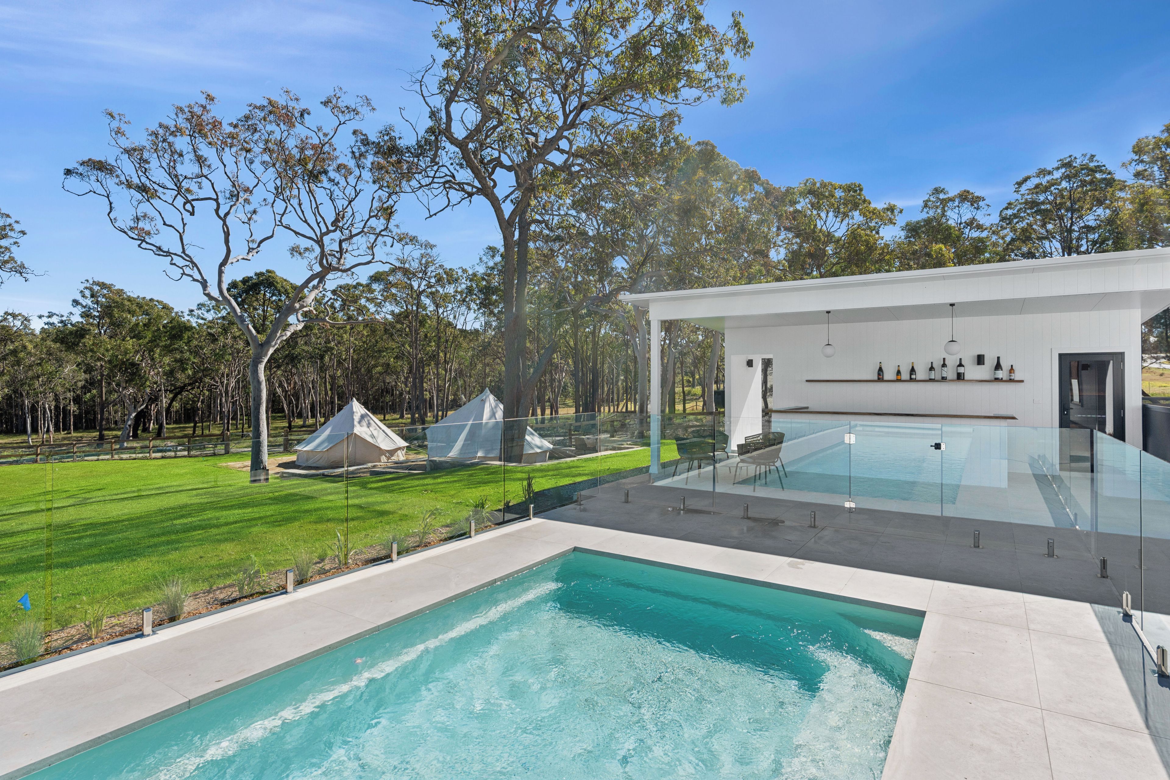 A modern outdoor pool area with a clear view of the surrounding landscape, including a grassy lawn and trees.