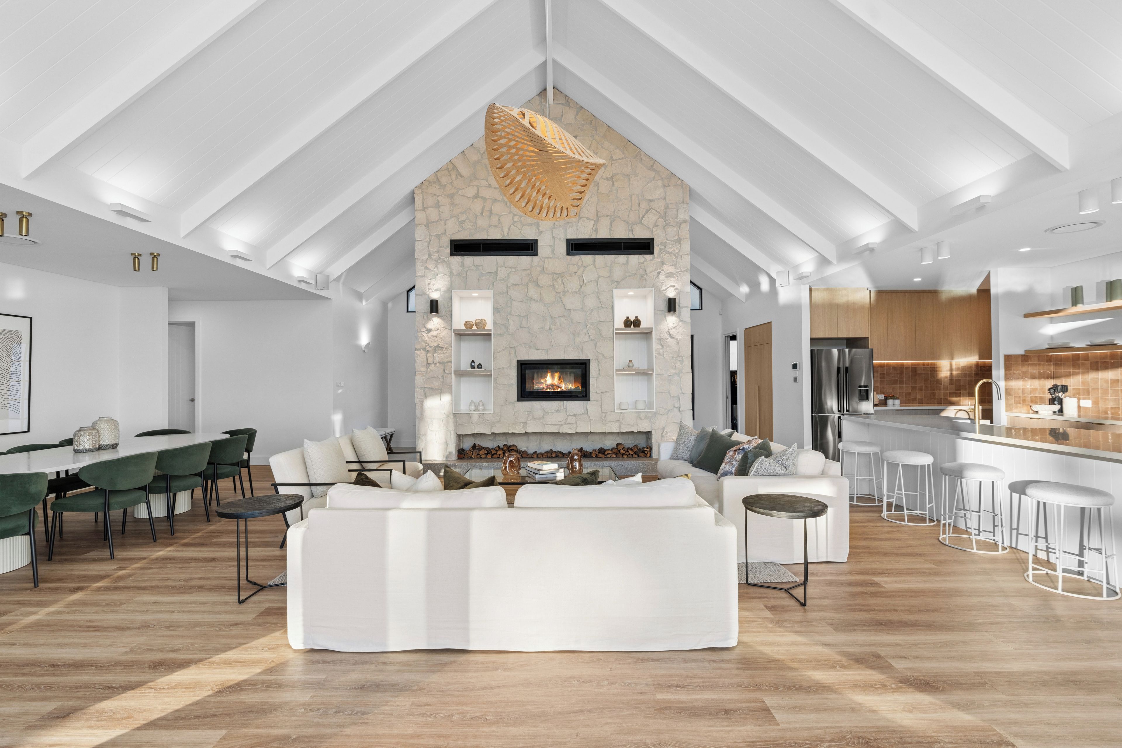 A spacious living area with a stone fireplace, a dining area with a long table, and a kitchen with modern appliances.