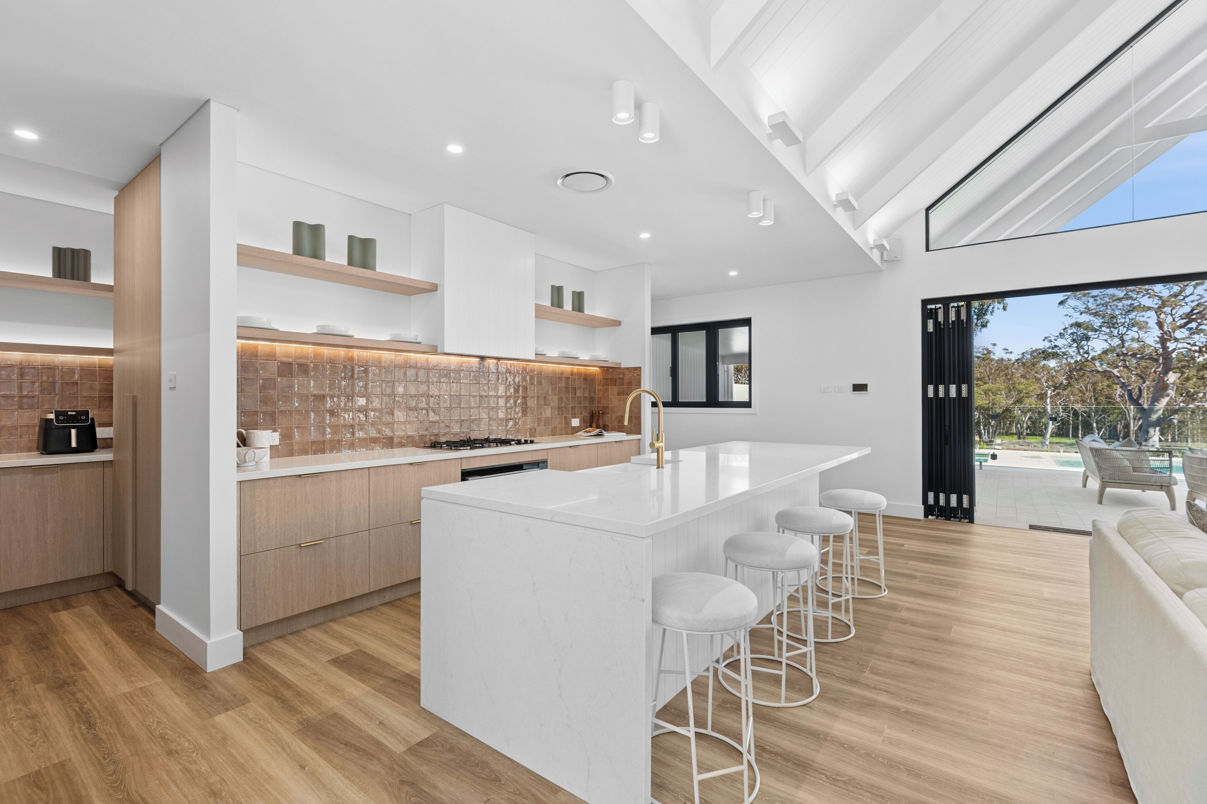 A modern kitchen with a central island, bar stools, and a view of the outdoors.