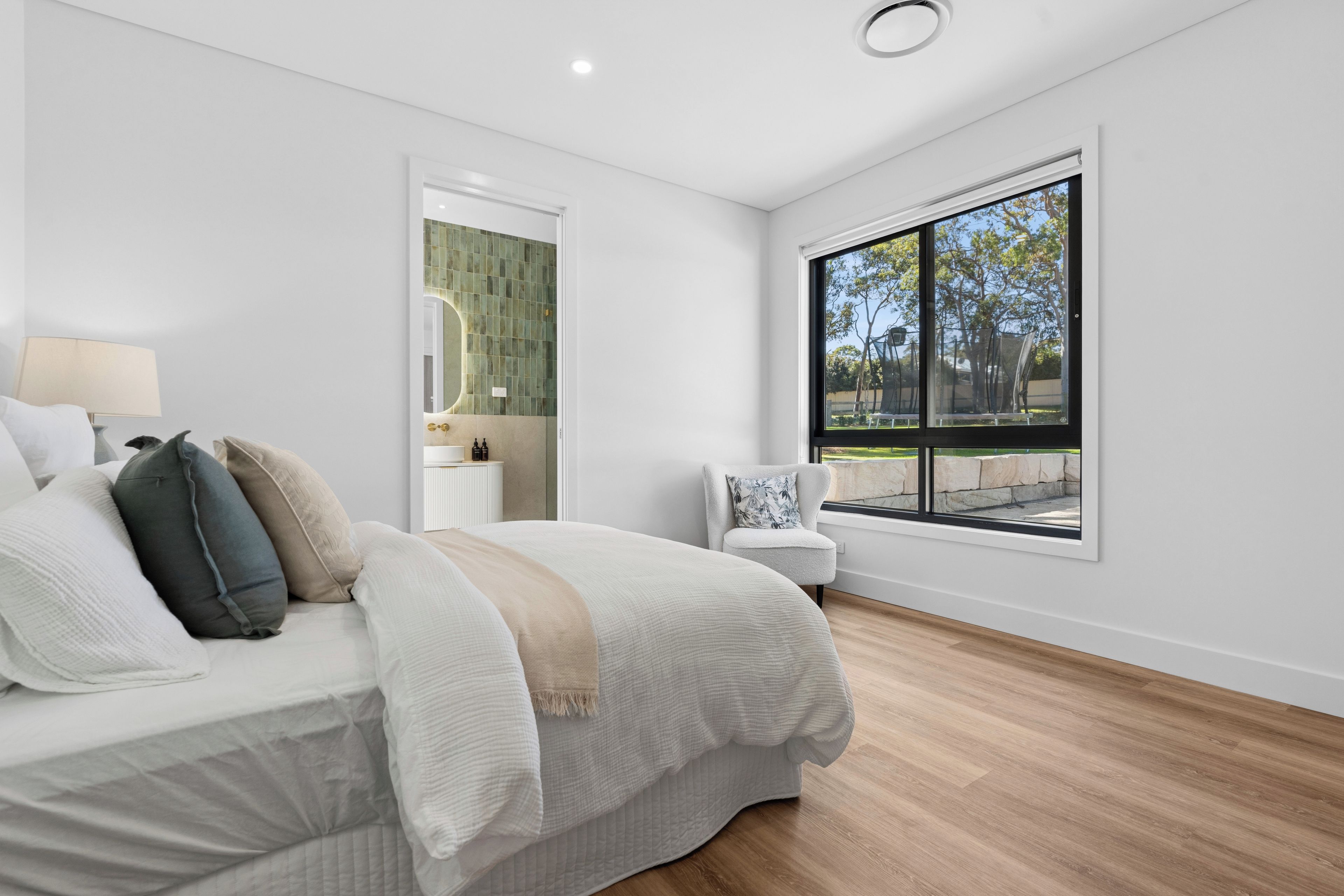 Un dormitorio moderno con una cama grande, una silla, un ventanal con vistas y una puerta que conduce a otra habitación.