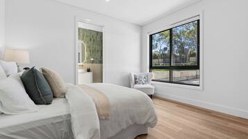 Un dormitorio moderno con una cama grande, una silla, un ventanal con vistas y una puerta que conduce a otra habitación.