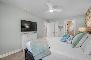 Ein Schlafzimmer mit einem Bett, einem Fernseher auf einem Schrank, einem Deckenventilator und einer Tür zu einem anderen Raum.