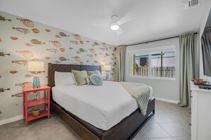 Een slaapkamer met een bed, nachtkastjes, een plafondventilator en een raam met gordijnen.