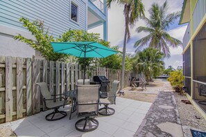 Een terras met een tafel, stoelen, een barbecue en een houten omheining.