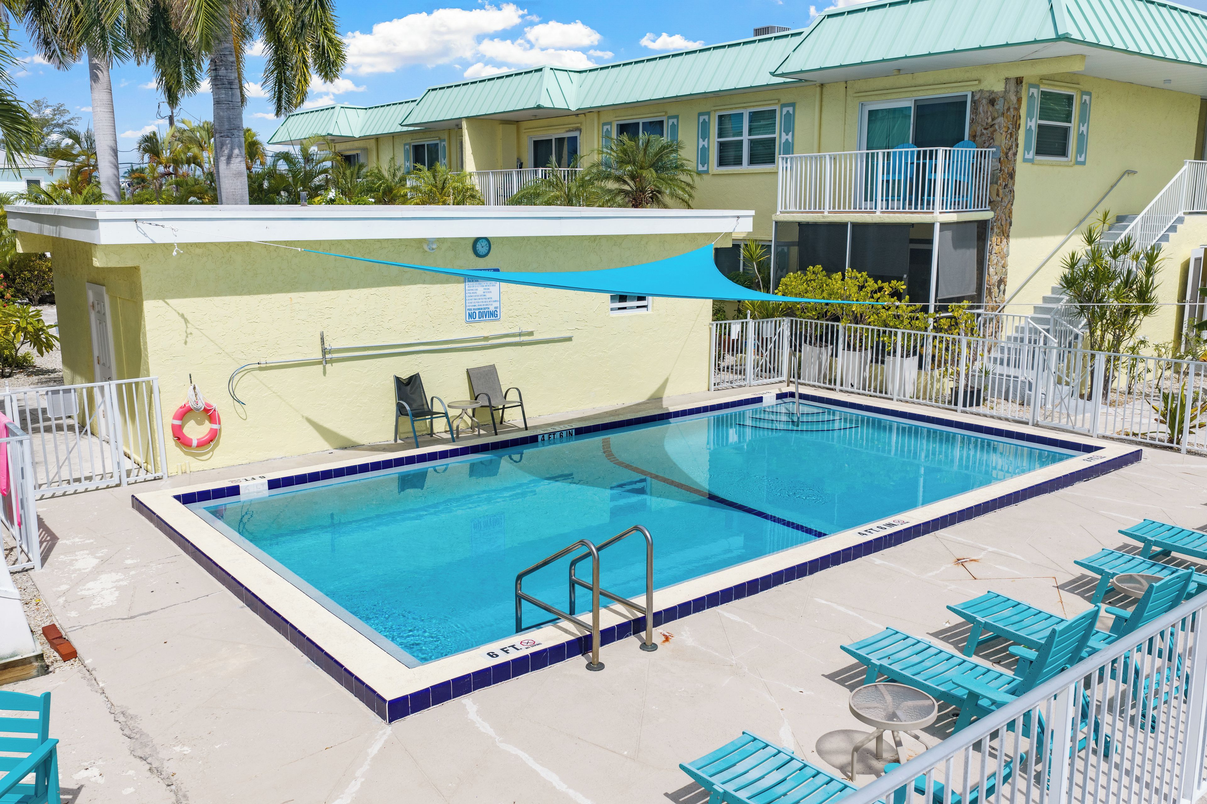 A swimming pool with a no diving sign, surrounded by lounge chairs and a covered area.