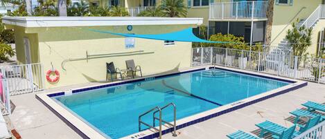 A swimming pool with a no diving sign, surrounded by lounge chairs and a covered area.