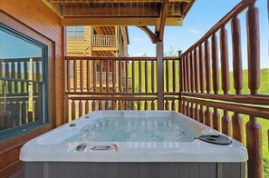 A hot tub on a wooden deck with a wooden railing and a building in the background. - Mountain Lookout – Incredible Mt. LeConte Views, Theater, Game Room, Sauna & Hot Tub (Gatlinburg)