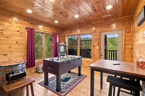 A wooden-floored room with a foosball table, a bar area, and a view of the outdoors. - Mountain Lookout – Incredible Mt. LeConte Views, Theater, Game Room, Sauna & Hot Tub (Gatlinburg)