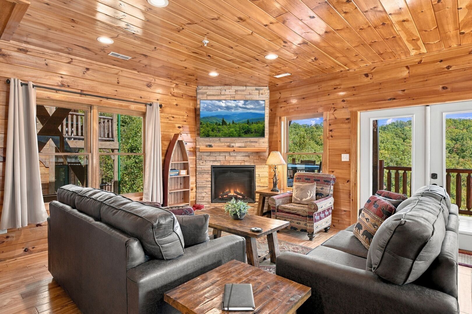 A cozy cabin interior with a fireplace, leather sofas, a wooden coffee table, and a bookshelf.