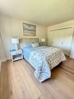 A bedroom with a bed, two bedside tables, a nightstand, a painting on the wall, and a wardrobe. - Newly Renovated 2 Bedroom Condo across the street from the Beach (Bonita Springs)