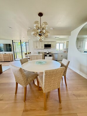 A modern kitchen with white cabinets, a central island, and a large round dining table with six chairs. - Newly Renovated 2 Bedroom Condo across the street from the Beach (Bonita Springs)