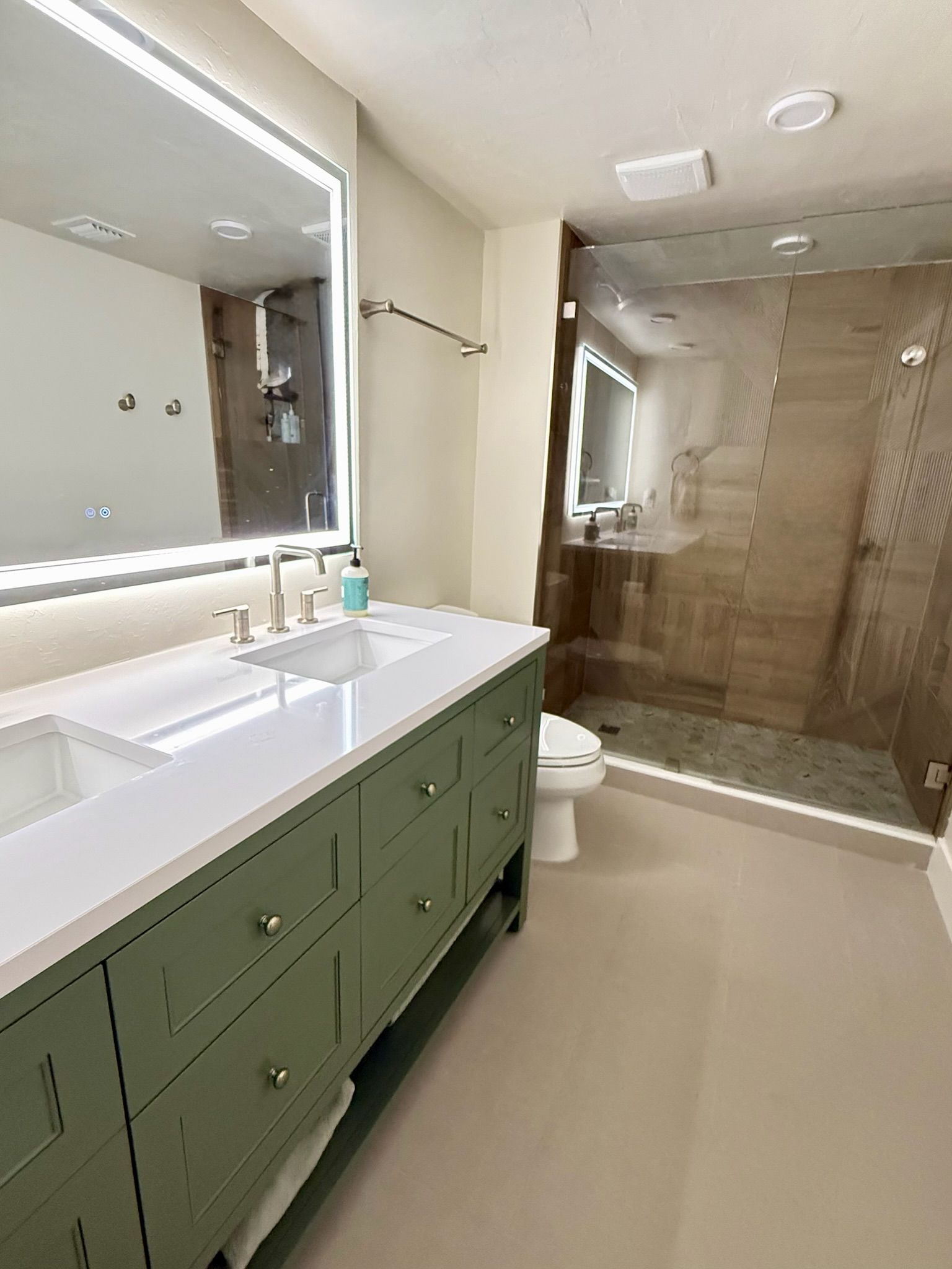 Une salle de bain avec un grand miroir, un lavabo, des toilettes et un espace douche.