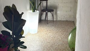 Un corridoio stretto con pavimento piastrellato, una sedia, una libreria piena di libri e una pianta in vaso.