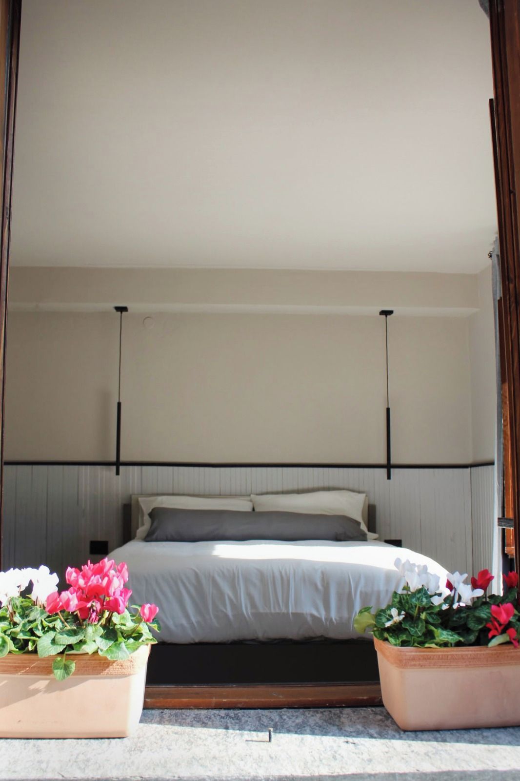 Un dormitorio con una cama, dos mesitas de noche, un cabecero y dos plantas en macetas.