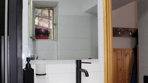 Un bagno con un lavandino bianco, un rubinetto nero e uno specchio sopra. Si vede una finestra con vista sull'esterno, e un porta asciugamani con un asciugamano bianco.