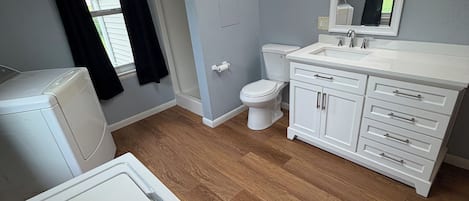 Ein Badezimmer mit einem weißen Waschtisch, einer Toilette und einem Fenster mit schwarzen Vorhängen.