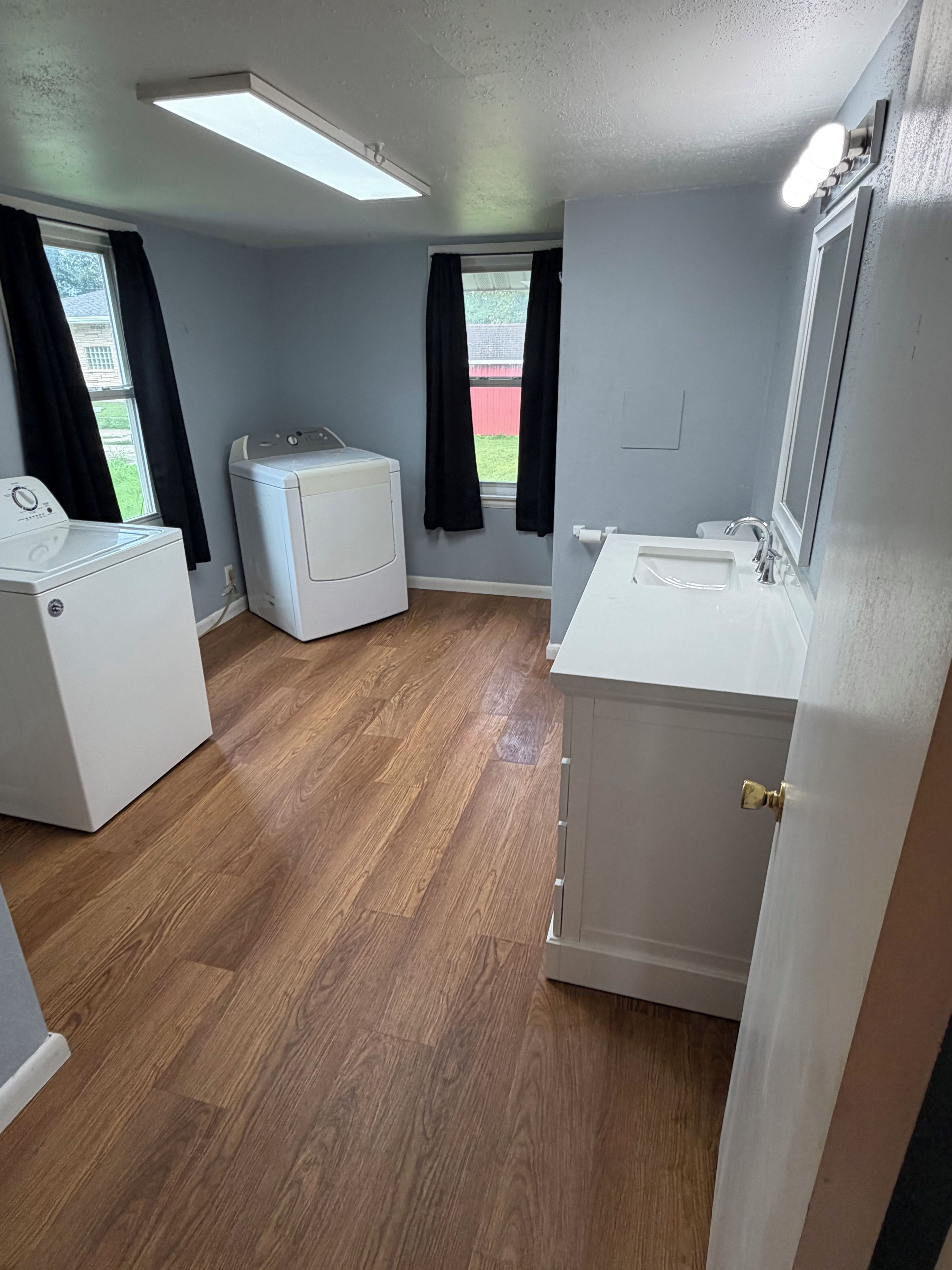 Un lavadero con dos lavadoras, un lavabo y una puerta que da a otra habitación.