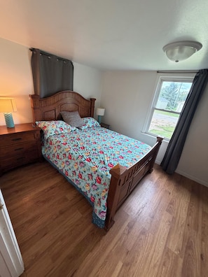 Un dormitorio con cama de madera, una mesita de noche, una lámpara y una ventana con cortinas.
