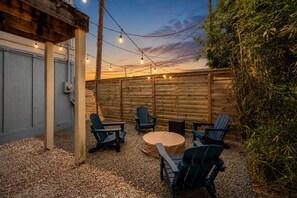 An outdoor patio with a wooden fence, string lights, and Adirondack chairs. - Galveston 4BR Getaway Game Room Sleeps 12 (Galveston)
