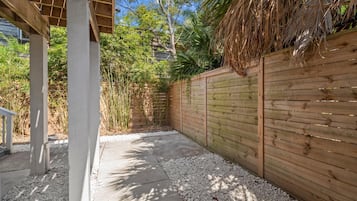 Área externa coberta com caminho de concreto, cerca de madeira e vegetação.