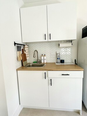 A compact kitchen with white cabinets, a stainless steel sink, and a wooden countertop. - Casita Near Little Havana with Parking (Miami)