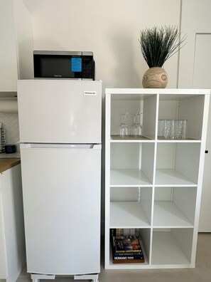 A white refrigerator with a Kenmore microwave on top, a white cabinet with shelves, and a vase with green plants. - Casita Near Little Havana with Parking (Miami)