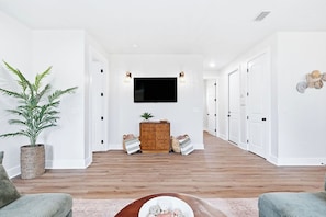 A modern living room with a flat-screen TV, a wooden cabinet, and a potted plant. - Pool, Sleeps 16, Outdoor Fun, Golf Cart, Fire Pit (Panama City Beach)