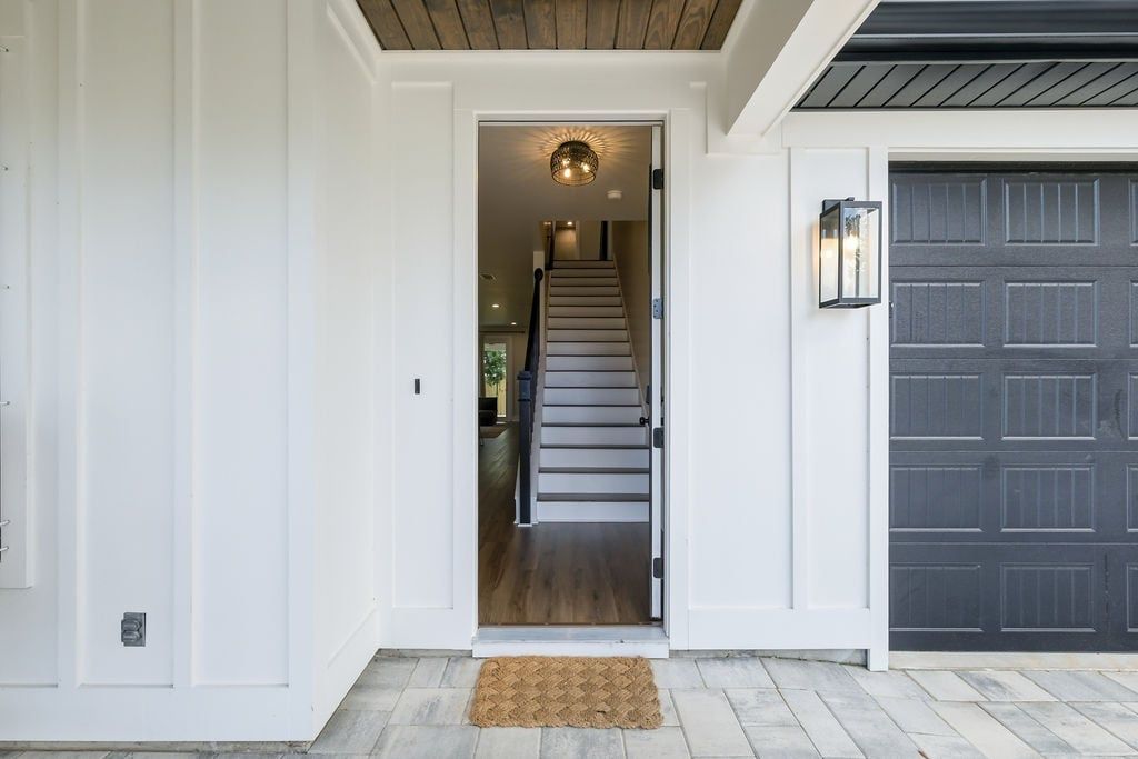 A front entrance with a staircase leading to an upper floor, a dark garage door, and a light fixture above the door.