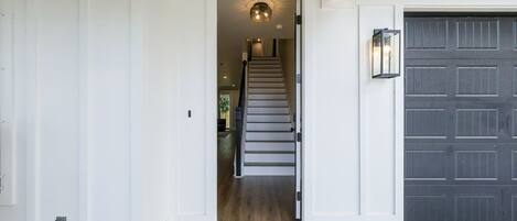 A front entrance with a staircase leading to an upper floor, a dark garage door, and a light fixture above the door.