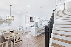 A modern kitchen with white cabinetry, a central island with bar stools, and a staircase with wooden steps. - Pool, Sleeps 16, Outdoor Fun, Golf Cart, Fire Pit (Panama City Beach)