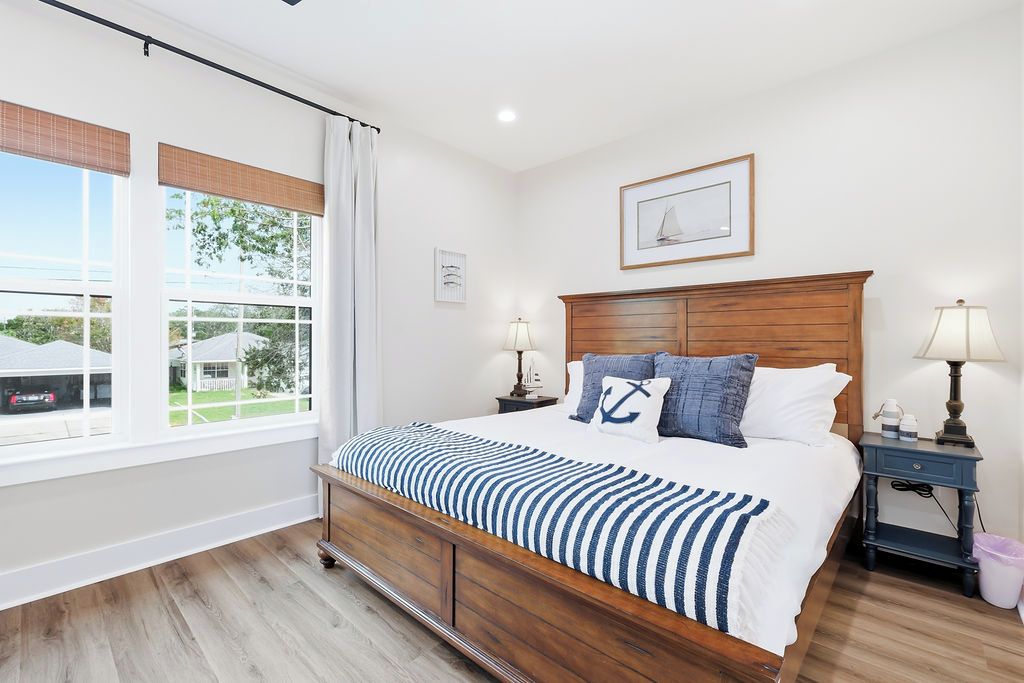 Un dormitorio con una cama de madera, dos mesitas de noche, un ventanal con persianas y un cuadro enmarcado en la pared.