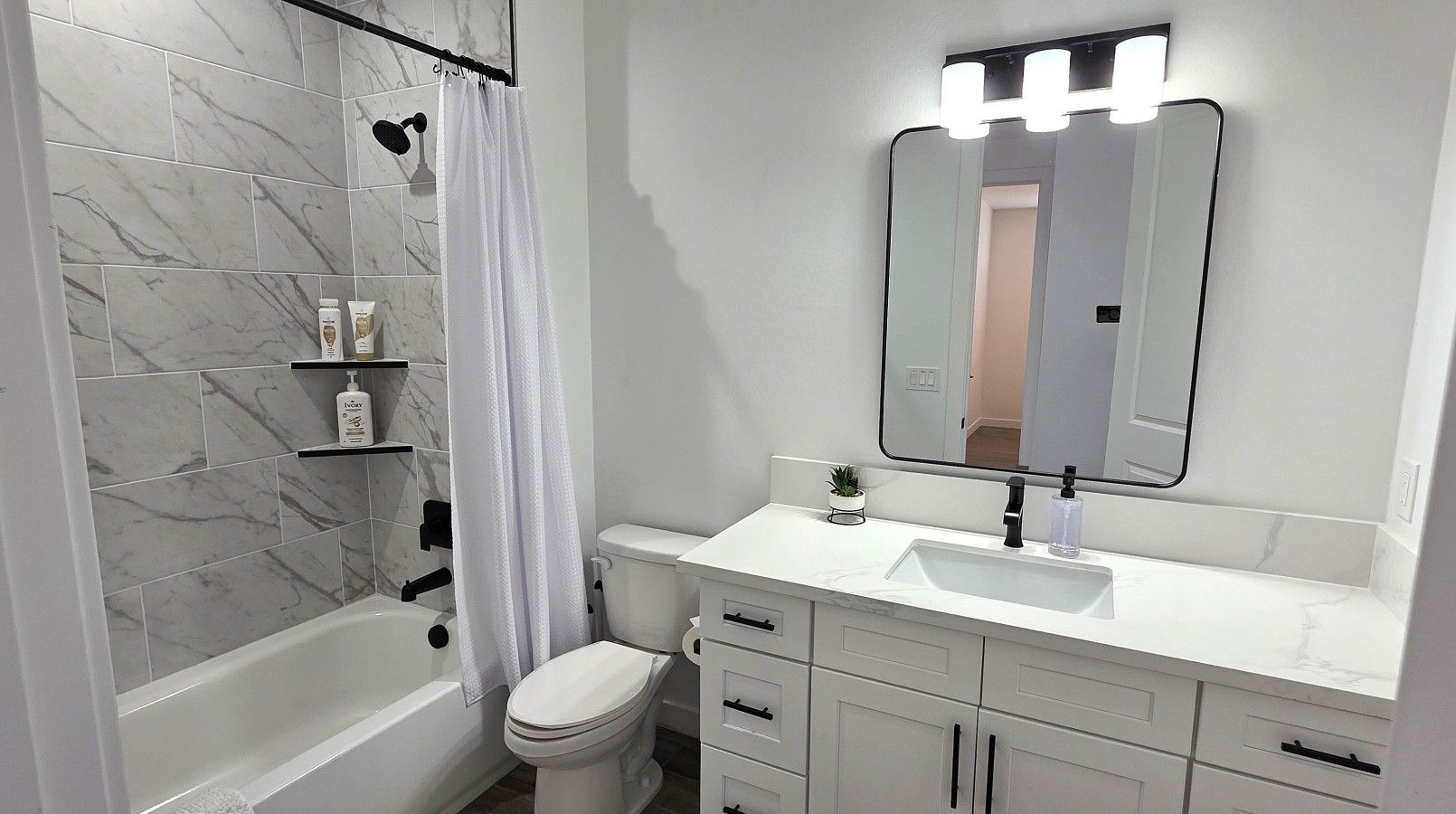 A bathroom with a bathtub, toilet, vanity with a mirror, and a shower curtain.