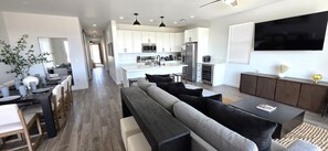 Una cocina moderna con armarios blancos, una isla central y un comedor con una mesa larga y sillas.