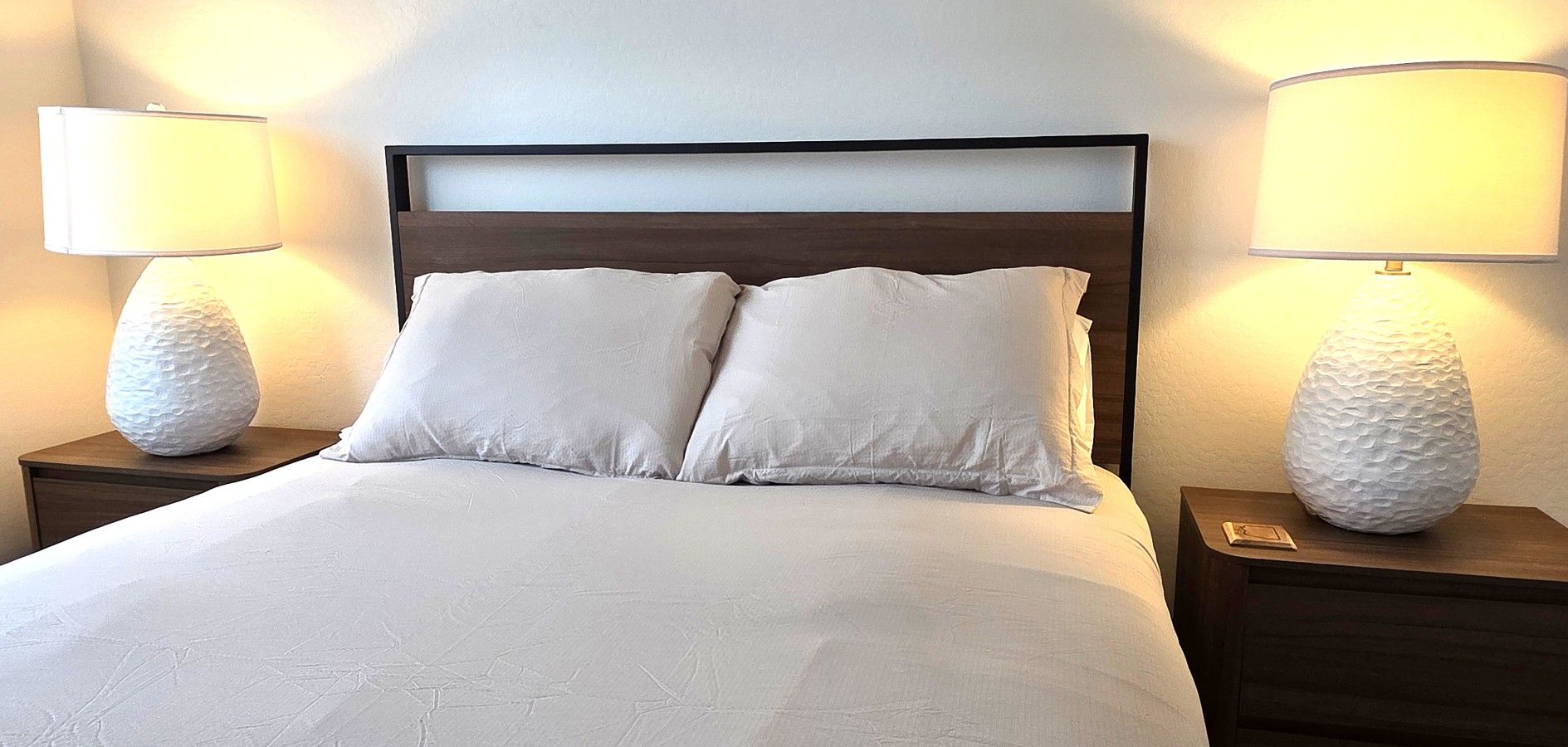A neatly made bed with two pillows and two bedside lamps on wooden nightstands.