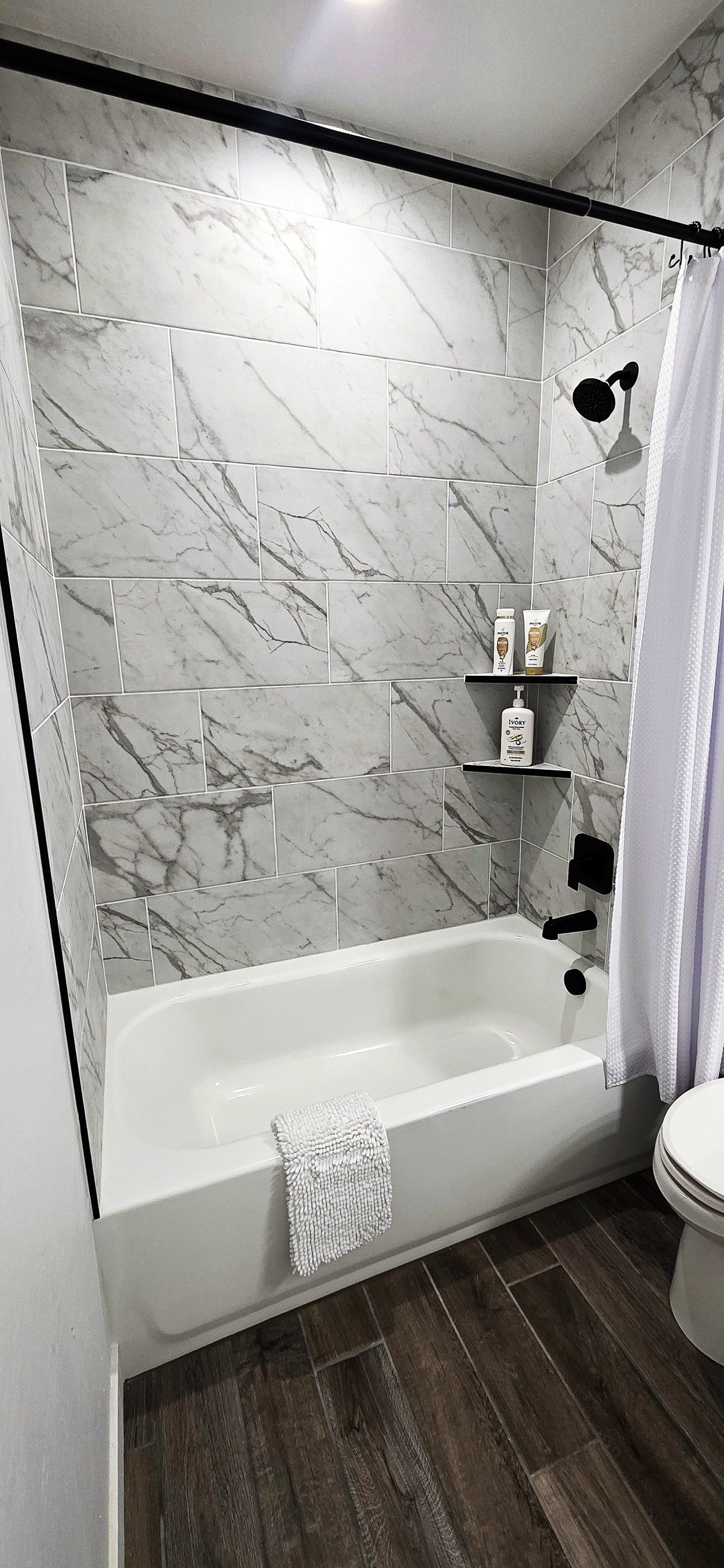 Een badkamer met een marmeren wand, een badkuip, een toilet en een douche.