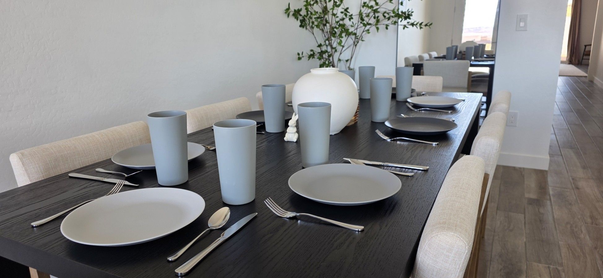 Une table à manger dressée avec des assiettes, des couverts et des verres gris, dans un intérieur moderne.