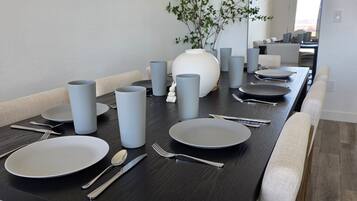 Une table à manger dressée avec des assiettes, des couverts et des verres gris, dans un intérieur moderne.