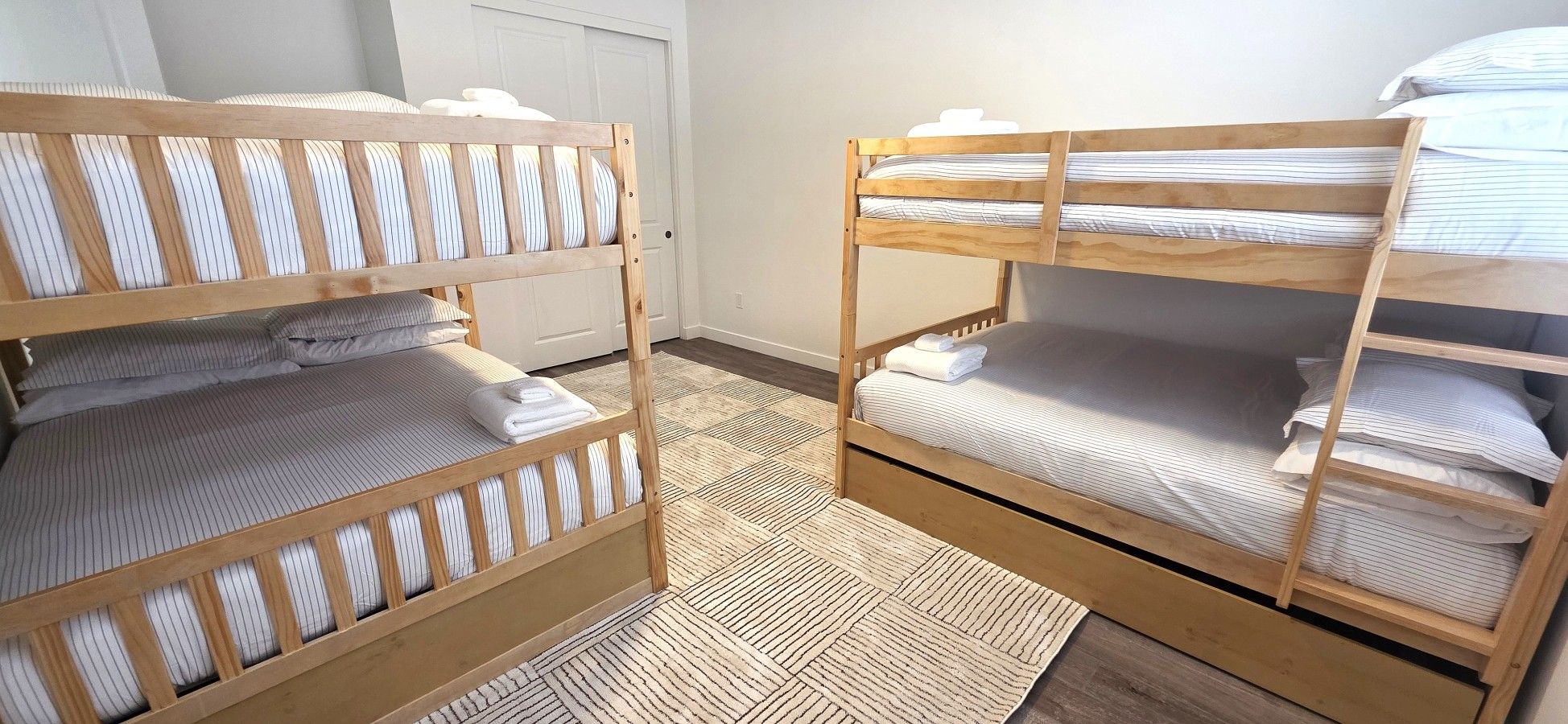 Een kamer met twee stapelbedden, een houten vloer en een witte deur op de achtergrond.